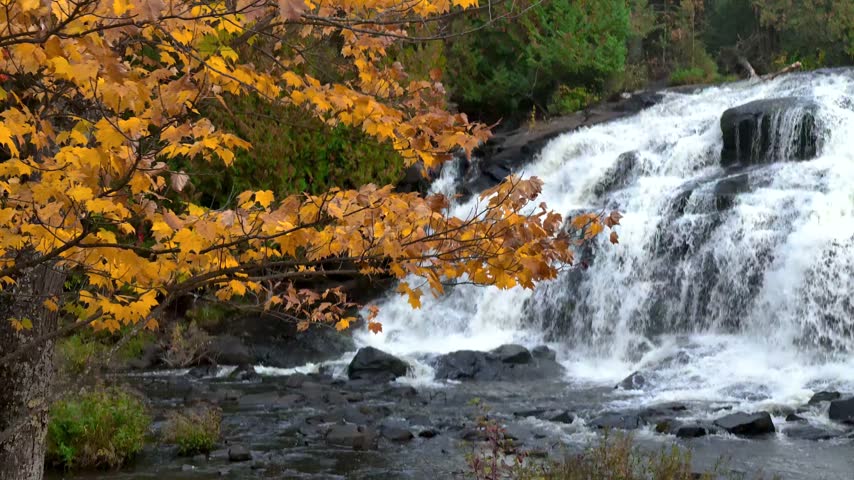 Powerful Bond falls cascading over rocks during a beautiful autumn day with colorful foliage in Michigan.