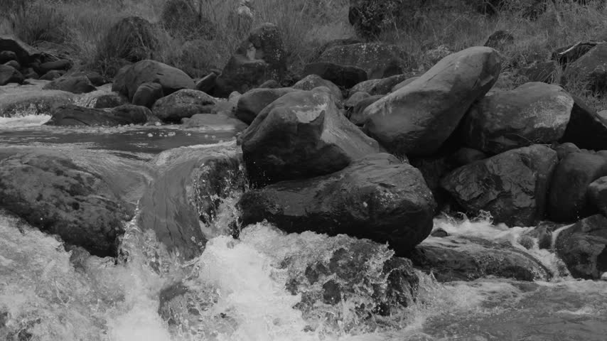 Black and white shot of water flowing over river rocks