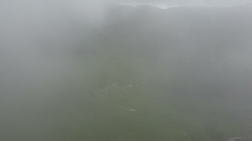 An expansive aerial perspective of rolling green hills with tea plantations and thick tropical forests enveloped in low-hanging clouds and fog, showcasing a serene highland landscape.