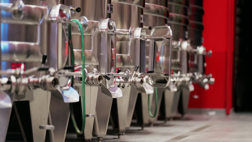Slow zoom out shot of stainless steel fermentation tanks in a modern winery facility with clean concrete floor.