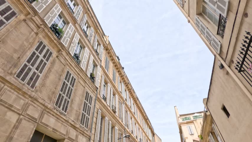 Camera moves through an old European street looking up at historic facades in Marseille, France.