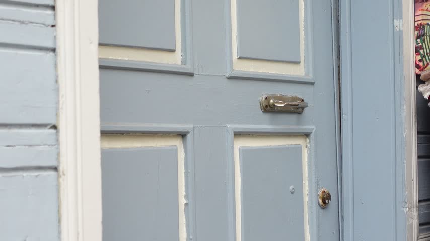Close up view of hand knocking on vintage blue painted wooden front door of home exterior. Person reaches out and taps firmly on door panel while waiting for someone to answer.