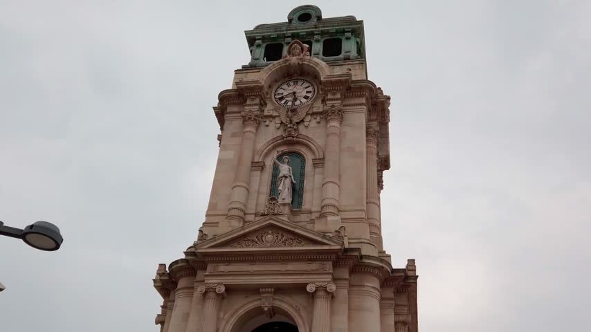 Historic Mexican church tower featuring an ornate facade with clock and religious statue. Detailed stone architecture and classical decoration create a striking urban heritage scene.