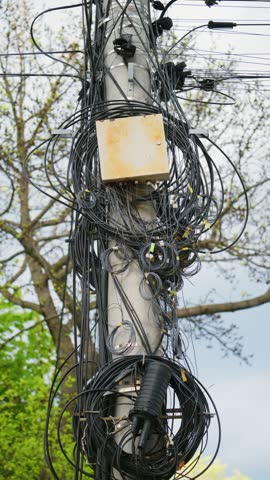 Complicated nest of black communication cables with junction box on utility pole. Dangerous urban infrastructure.