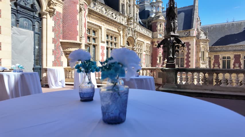Elegant outdoor table setting with blue floral arrangements against the ornate courtyard of Palais Bénédictine in Fécamp, Normandy, France