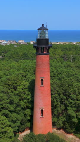 Upper Section Of Red Brick Currituck Beach Lighthouse Against Green Forest Canopy And Distant Atlantic Ocean Shoreline In Corolla, North Carolina, United States. - aerial vertical shot