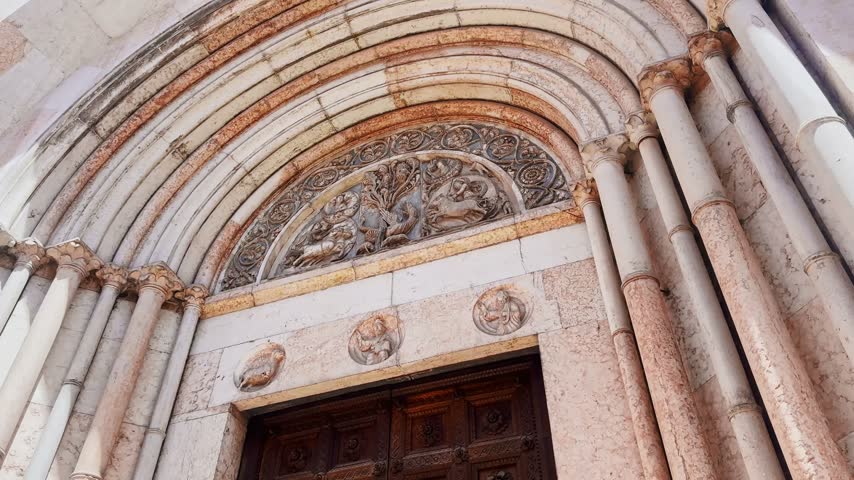 Close-up of the Baptistery of Parma entrance, revealing a Romanesque marble portal, sculpted tympanum, slender columns and richly decorated medieval stonework.