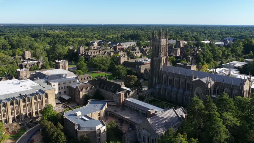 Duke Chapel and its Gothic quad sit in the foreground over Durham, North Carolina, a cluster of medical and research towers visible on the skyline behind. Aerial view