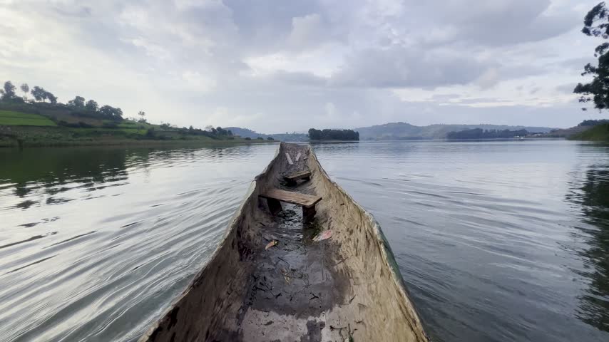 Traditional wooden dugout canoe viewed from the bow on Lake Bunyonyi, southwestern Uganda, with calm water, wooded islands and Kigezi Highlands beyond, first person POV.