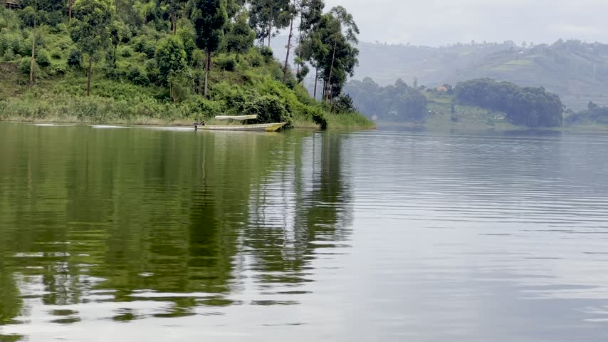 Passenger boat journey across Lake Bunyonyi in Kabale District, southwestern Uganda, with forested shores, cultivated hills and small islands reflected in calm water, first person POV.