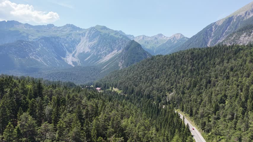 Tirol mountain valley stretches toward rocky alps near Biberwier, Austria, aerial drone push over dense forest, road and peaks.