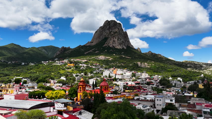 An aerial perspective of the massive Pena de Bernal monolith towering over a colorful colonial town in Queretaro, Mexico. Perfect for travel documentaries and cultural heritage content.
