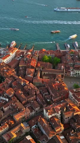 Cinematic aerial footage captures sunlight glowing over classic Venetian architecture with ferry traffic on water channel.