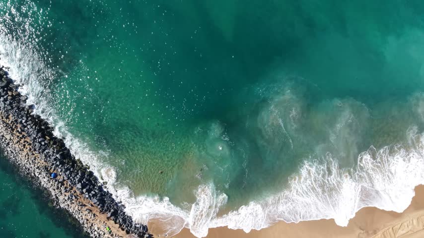 A Birds-Eye-View Captures the Blue Green Waves of the Pacific Ocean crashing down on the Sandy Shore of Newport Beach California.