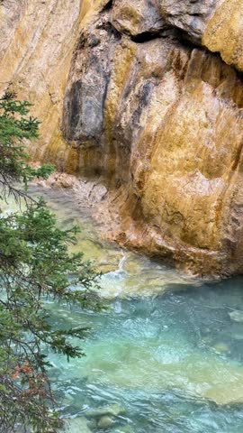 A turquoise glacial creek winds beneath towering ochre-stained cliffs at Johnston Canyon in Banff National Park, Alberta, a colorful canyon in the Canadian Rockies.