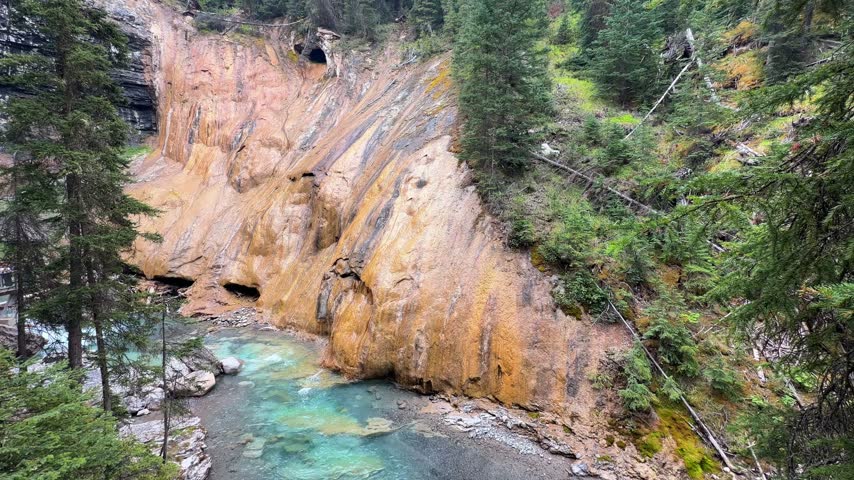A turquoise glacial creek winds beneath towering ochre-stained cliffs at Johnston Canyon in Banff National Park, Alberta, a colorful canyon in the Canadian Rockies.