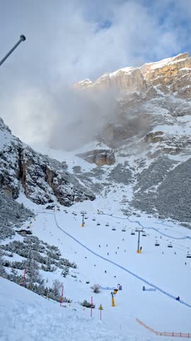 Scenic view of alpine ski resort with chairlifts and people skiing down mountain slopes under foggy rocky peaks during winter holiday season.