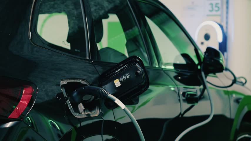 Black electric car plugged into charging station for power supply inside clean modern garage environment.