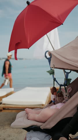 Baby sitting in stroller under bright red beach umbrella by the sea