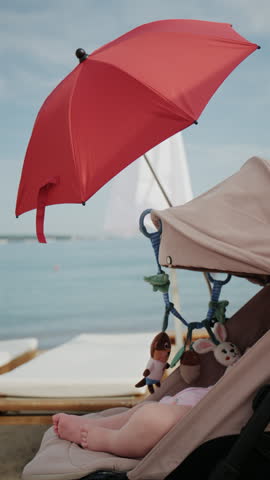 Baby sitting in stroller under bright red beach umbrella by the sea