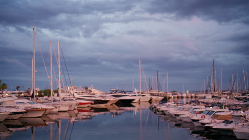 Atmospheric dusk view of Port Vauban Marina in Antibes, France, with rows of boats, sailboat masts, soft reflections, and a cloudy blue evening sky