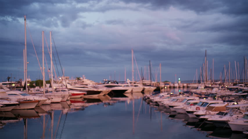 Atmospheric dusk view of Port Vauban Marina in Antibes, France, with rows of boats, sailboat masts, soft reflections, and a cloudy blue evening sky