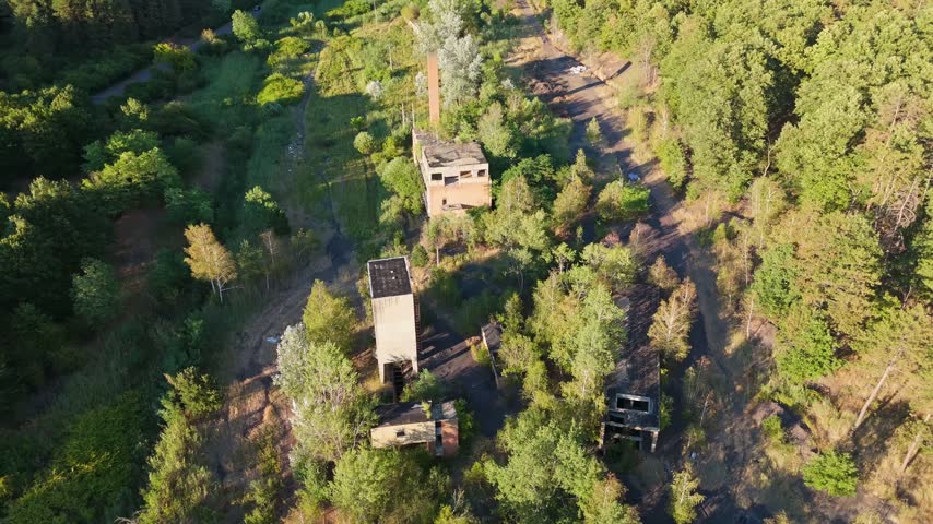 Aerial view of an abandoned coal loading facility and industrial ruins surrounded by summer forest in Rákóczibánya, Hungary, within the Mátra Mountains.