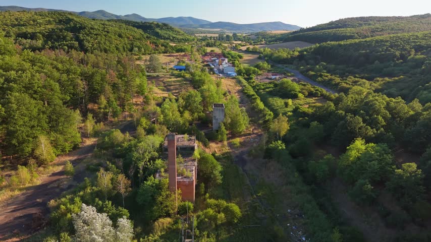 Aerial view of abandoned coal-loading facility ruins and concrete towers amid summer forest and rolling hills near Rákóczibánya, Hungary, in the Mátra Mountains.