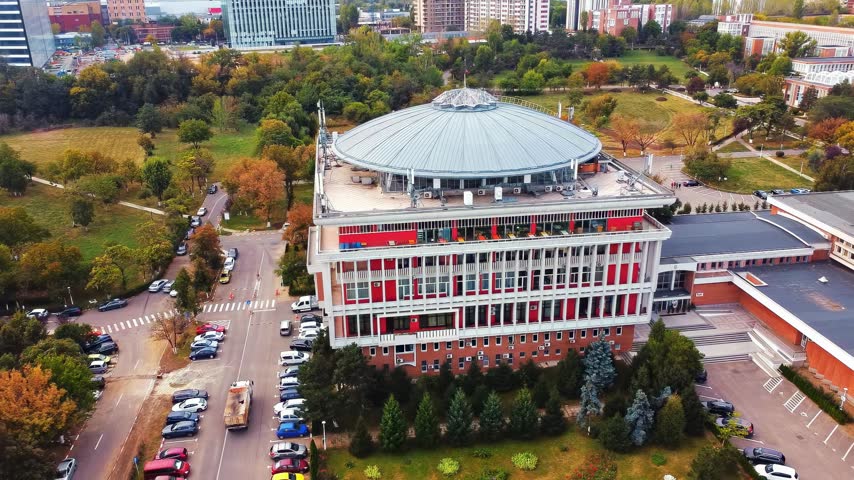 Cinematic aerial view of modern circular architecture university library building surrounded by vibrant autumn trees.