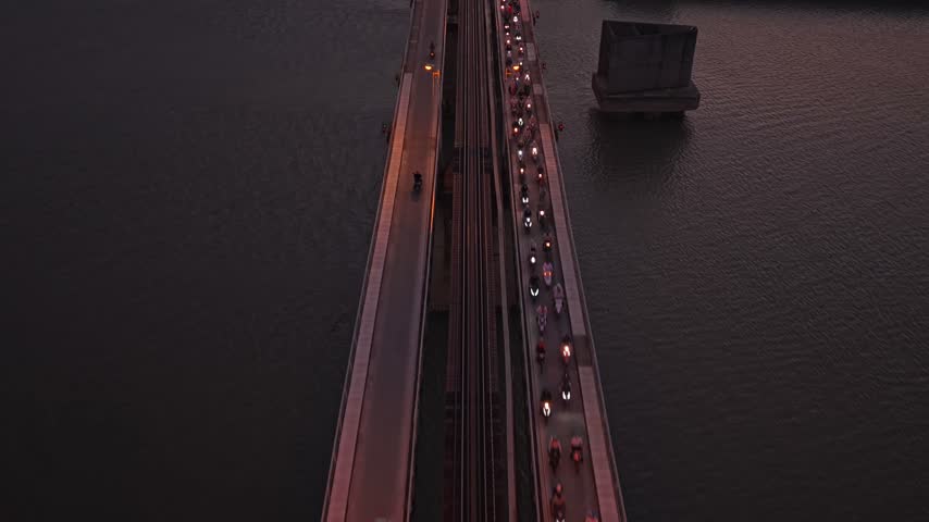 Dramatic aerial perspective following traffic on the historic long bien bridge crossing the red river during a vibrant sunset in hanoi, vietnam