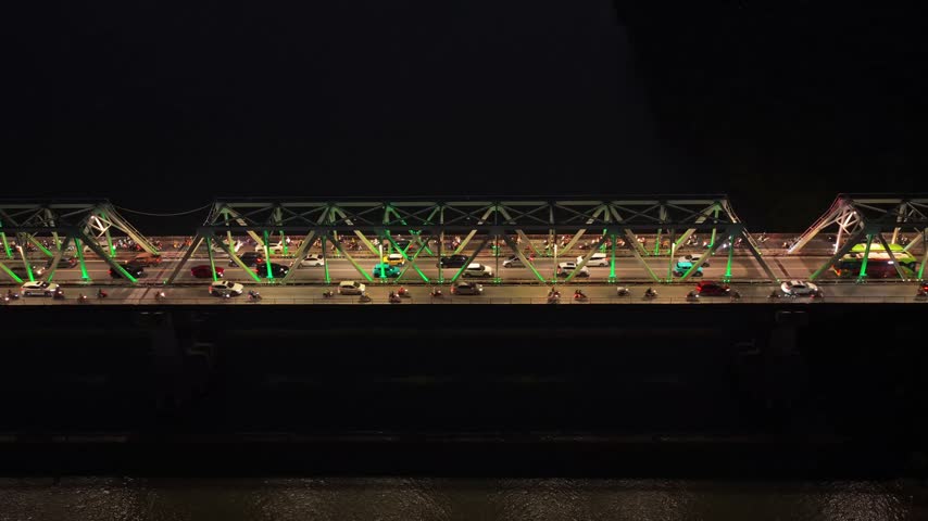 Striking aerial view of the illuminated cau chuong duong bridge in hanoi, vietnam, showing busy nighttime traffic with cars and motorcycles