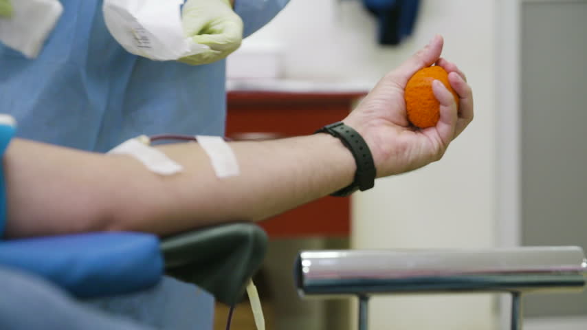 Bright indoor clinic light illuminating a patient squeezing an orange ball during donation.