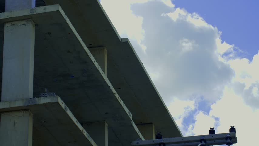 A low angle shot of a column wrapped in blue plastic sheeting against white cumulus clouds