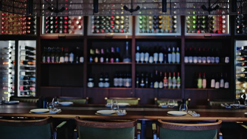 Sophisticated upscale restaurant dining area featuring wooden table place settings and out of focus wall mounted wine racks.