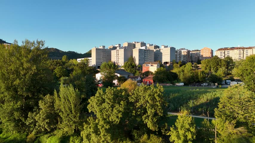 Aerial perspective revealing the Quintela neighborhood with its buildings surrounded by lush green trees and a clear blue sky in Ourense