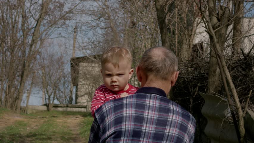 A grandfather holds his grandson in his arms as they walk through the woods. They enjoy nature and share a special moment together in the fresh air.