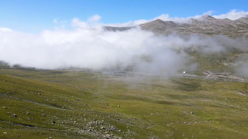 Footage of alpine meadows above tree line and cloudy blue sky.