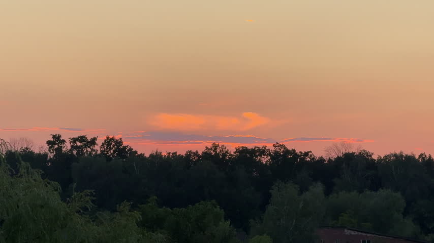 Beautiful sunset sky with glowing orange clouds over dark forest tree line silhouette