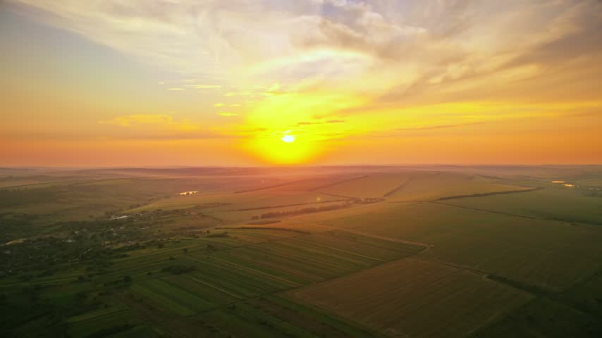 Dramatic sunset over vast farmland hills. Cinematic drone shot of sunrise glowing over countryside meadows and valley.