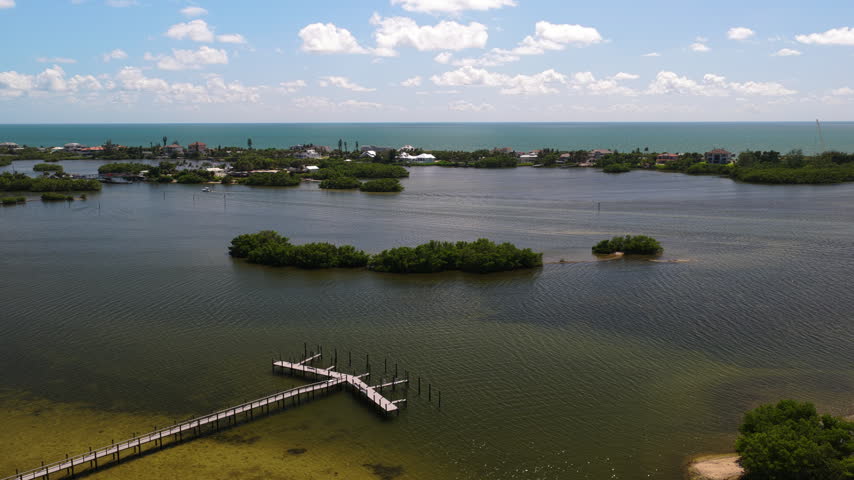 Mangrove islets sit in shallow coastal water beside wooden docks, with waterfront buildings and the open sea beyond.