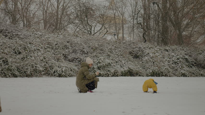 In a winter wonderland, a young mother captures joyful moments while playing in the snow with her child at the park. They explore the beauty of winter together.