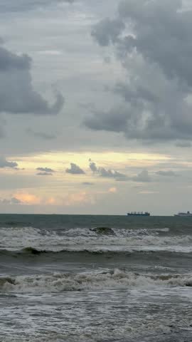 Rough sea waves crashing on the shore with white foam under a cloudy, overcast sky during twilight. Powerful ocean movement and dramatic nature landscape background.. 4k video.