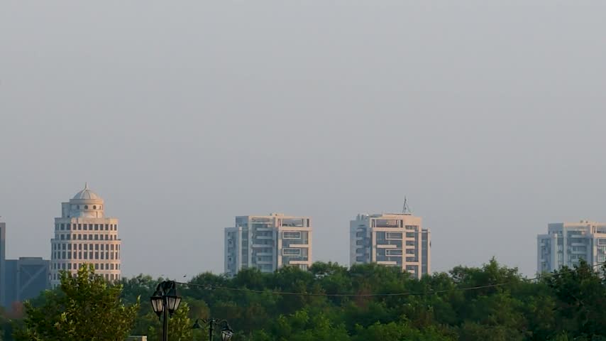Modern high-rise buildings rise above dense green trees in the New Blue Area of Islamabad, Pakistan
