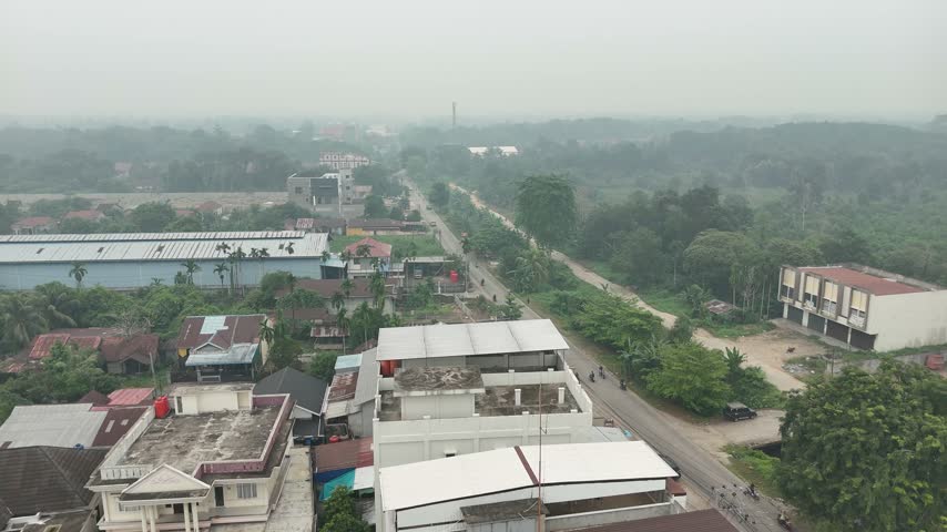 An aerial view of a street in a small town that runs through a residential and industrial area, with a misty green landscape.