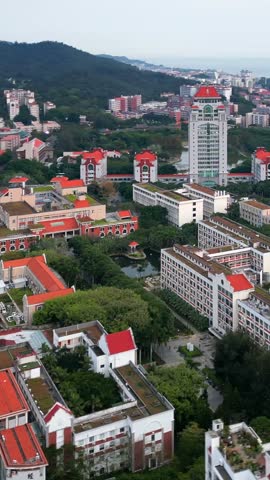 Stunning aerial view of Xiamen University, showcasing its beautiful campus with red-roofed buildings nestled among lush greenery, overlooking the sea.