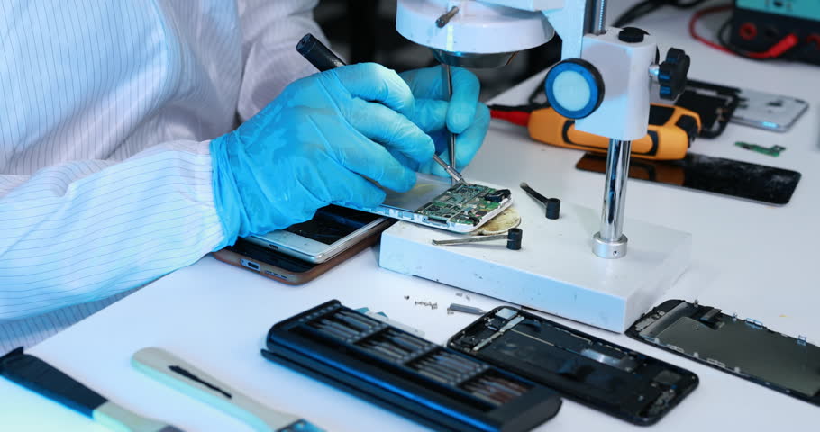 Close-up of a technician in blue gloves repairing a smartphone circuit board with precision tools under a microscope at an electronics workbench.