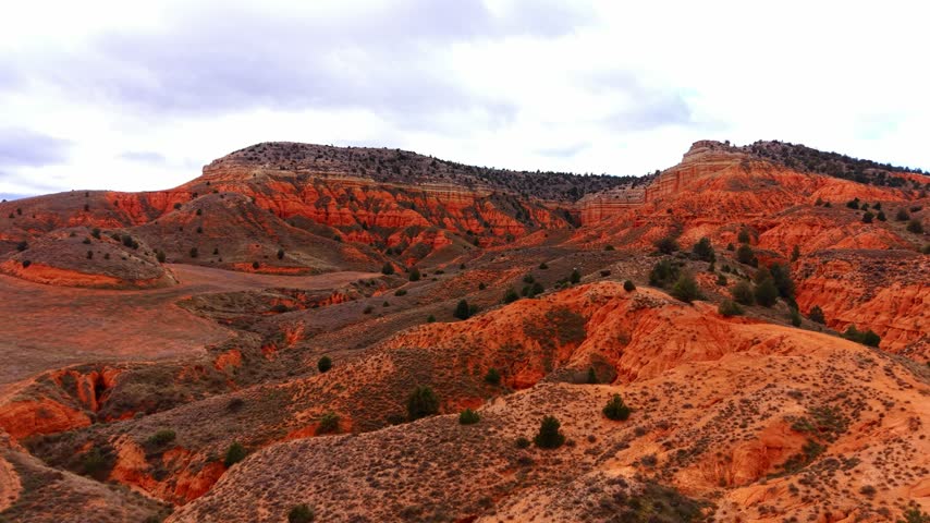 Canyon landscape with red rocks and green shrubs under a cloudy sky. A canyon with red rock formations and patches of green shrubs. The sky is mostly cloudy.