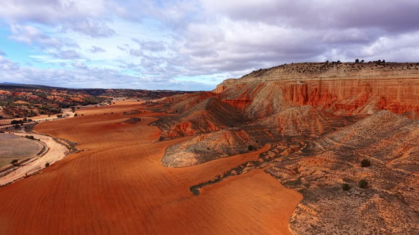 Bright red landscape with curved hills under a cloudy sky. The scene shows a wide, open area with red soil and hills in the background.