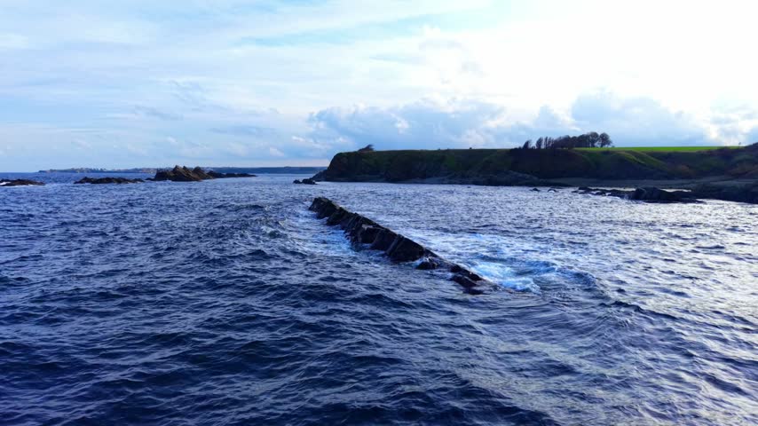 Waves crash on rocks in the coastal area during late afternoon. Waves hit the rocky surface near the shore as the sun begins to set on the horizon.