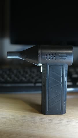 A black portable electric air duster standing on a desk.